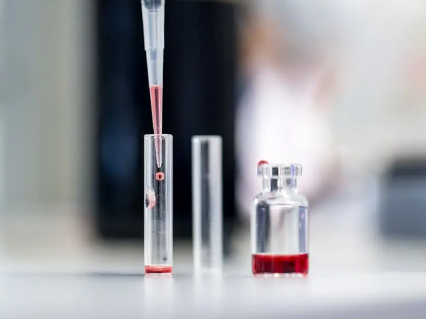 Pipette, die rote Flüssigkeit in ein Röhrchen tropft. 