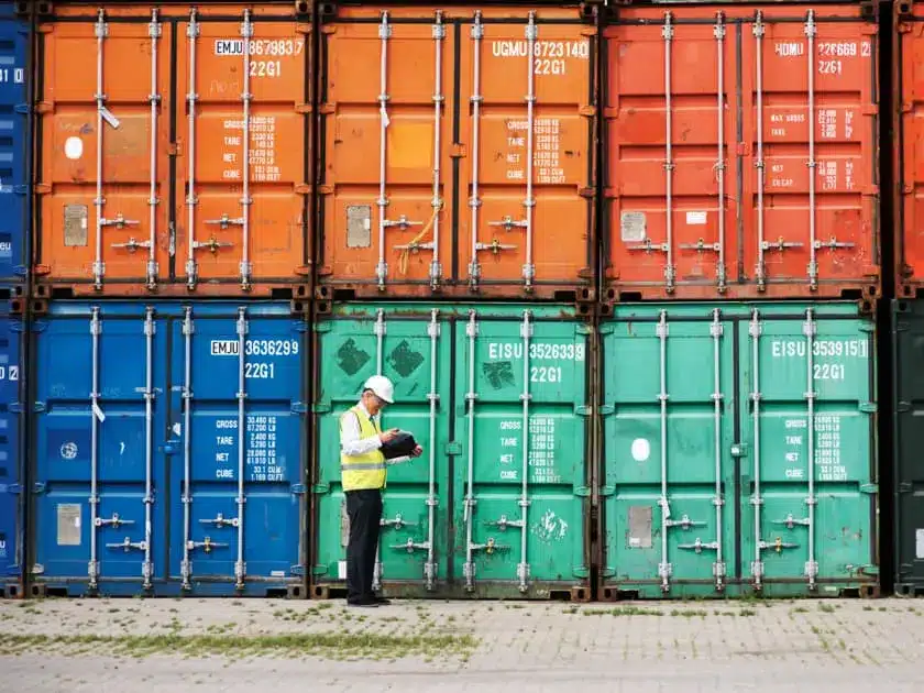 Mann in Warnweste vor gestapelten Containern. 